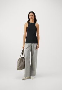 Un haut sans manches noir associé à un pantalon large à carreaux gris clair. Le modèle tient un sac gris doux avec des anses noires, portant des baskets blanches.