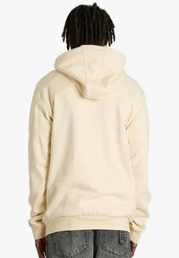 Felpa beige con cappuccio in tessuto morbido e strutturato. Dotata di tasca a marsupio e polsini a coste, presenta una vestibilità comoda e un design casual.