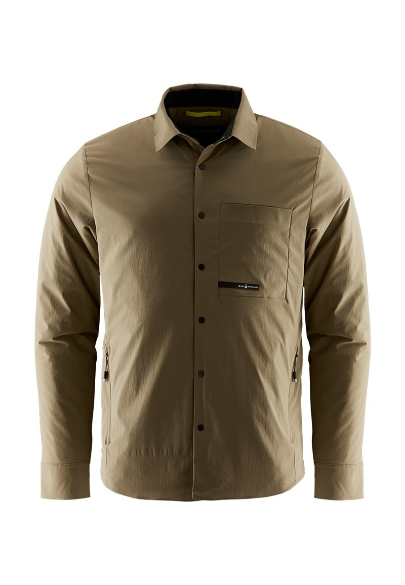Brun langærmet skjorte med knaplukning foran, en brystlomme og sidelommer med lynlås. Stoffet ser glat ud med en let tekstur.