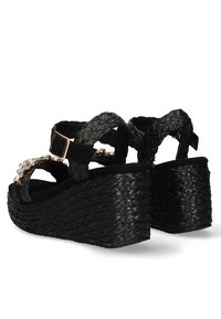 Sandalias de cuña negras con tiras trenzadas, adornadas con un acento decorativo. Textura tejida y color negro sólido en todo el diseño.