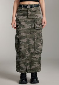 Lang nederdel med camouflage-mønster i grøn og grå stof, med sidelommer og en lynlåslomme. Kombineret med sorte, chunky sneakers.