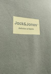 Jack & Jones ruhacímke szürke szöveten, alatta a márkanévvel nyomtatva a „Definition of Denim” szöveg.