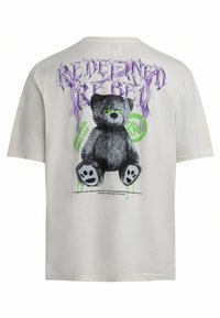 Cremfarbener Baumwoll-T-Shirt mit einem Grafikdesign eines schwarzen Teddybären mit grünen Akzenten und lila Text auf dem Rücken, der "REDEEMING REBEL" liest.