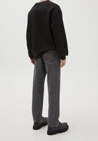 Sweatshirt noir à manches longues, associé à un jean gris droit. Des chaussures noires complètent la tenue. Accent sur un style décontracté et confortable.