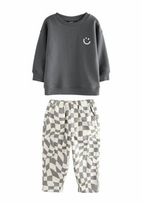 Szary sweatshirt z grafiką uśmiechniętej buźki i ściągaczami, w parze z białymi i szarymi spodniami w kratkę, które mają dwie boczne kieszenie.