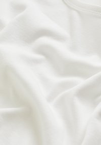 Weißer Baumwollstoff mit einer glatten Textur, der weiche Falten und Knitter zeigt. Leicht und luftig, geeignet für Bekleidung oder Polsterung.