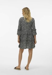 Vestido negro con flores de diseño escalonado, mangas tres cuartos y puños con volantes. Tejido ligero con un patrón de flores blancas por todo el vestido.