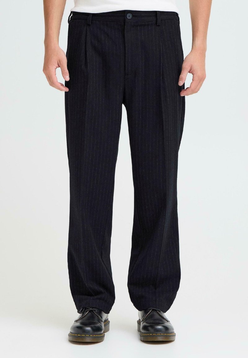 Donkere gestreepte broek van soepele stof, met een relaxte pasvorm en een knoopsluiting. Draag ze met zwarte schoenen.