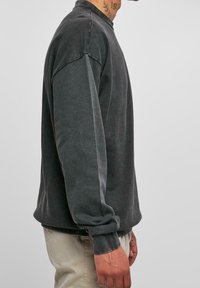 Sudadera gris de gran tamaño con mangas largas y cuello redondo, elaborada con una tela suave. Presenta un ajuste holgado y puños acanalados.