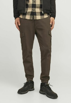 Bruine cargobroek met elastische boorden en zijzakken, gecombineerd met zwarte sneakers. De stof is duurzaam en heeft een gladde textuur.
