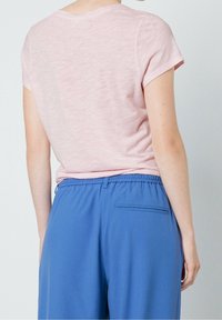 Jasnoróżowa, krótko rękawowa koszulka o miękkiej fakturze, w połączeniu z niebieskimi spodniami na elastycznej talii z tylną kieszenią i luźnym krojem.