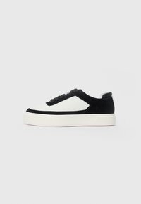 Lage sneaker van zwart suede met witte leren panelen, zwarte veters en een dikke witte rubberen zool, weergegeven vanaf de buitenzijde.
