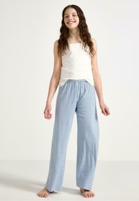 Weißes, ärmelloses Oberteil kombiniert mit hellblauen, lockeren Hose mit dünnen Streifen und elastischem Bund.