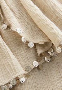 Tissu beige texturé avec de petites sequins métalliques ronds comportant des motifs étoile et lune découpés le long des bords.