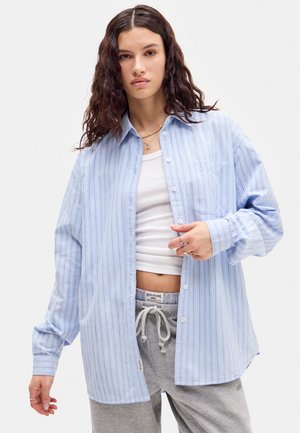 Himmelblau gestreifen Hemd mit Knöpfen und einer Brusttasche, kombiniert mit einem weißen Tanktop und grauen Sweatpants mit Kordelzug.