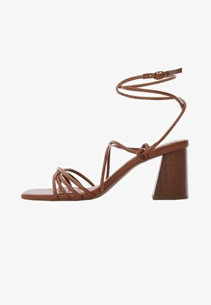 Sandales brunes à talon carré épais, fines lanières croisant le pied et une bride à la cheville pour un ajustement sécurisé. Matière lisse et élégante.