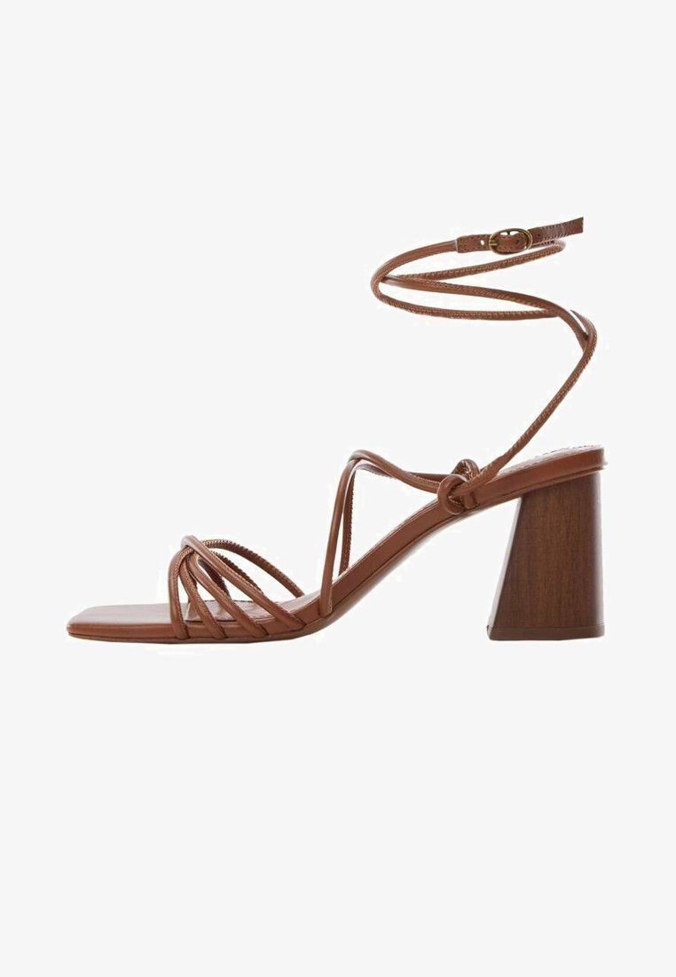 Sandales brunes à talon carré épais, fines lanières croisant le pied et une bride à la cheville pour un ajustement sécurisé. Matière lisse et élégante.