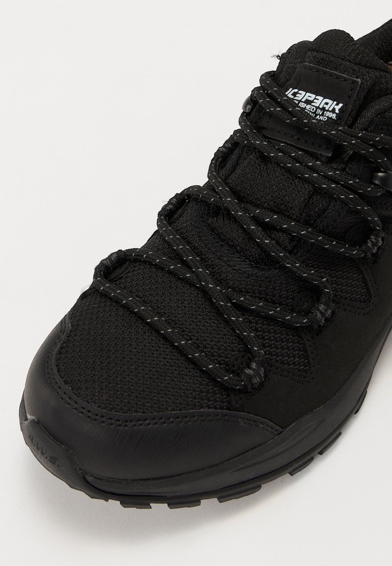 Czarny but sportowy z teksturowaną siateczką na cholewce, okrągłymi sznurowadłami z odblaskowymi nićmi oraz wytrzymałą gumową podeszwą.