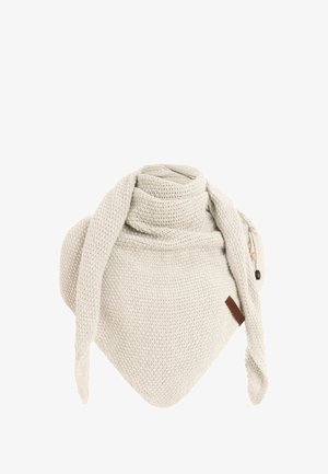 Knitted cream scarf with a triangular shape and ties, featuring a textured pattern and a small brown leather tag as an accent detail.