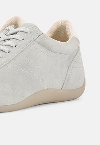 Ανοιχτό γκρι σουέντ αθλητικό παπούτσι με χαμηλό προφίλ, υφασμένο επάνω μέρος, επίπεδα κορδόνια και ελαφριά ταμπά λαστιχένια σόλα. Διαθέτει διακριτικές λεπτομέρειες ραφών.