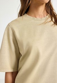 Beige bomulds T-shirt med rund hals, korte ærmer og en afslappet pasform. Stoffet har en blød tekstur og minimalistiske syninger.