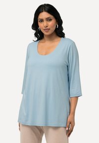 Helles blaues Langarmoberteil mit U-Ausschnitt. Aus weichem Stoff gefertigt, bietet es eine lockere Passform und seitliche Schlitze für zusätzlichen Komfort.