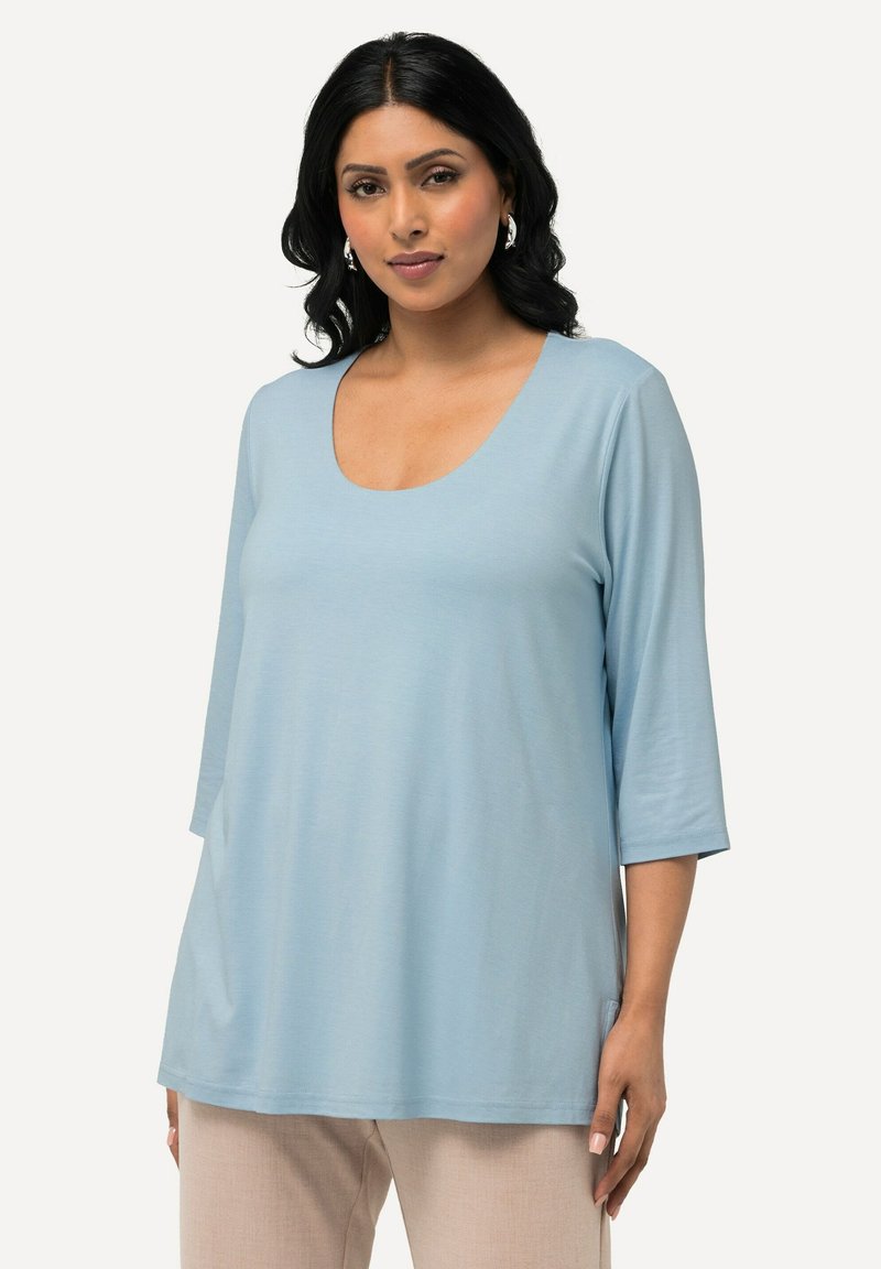 Helles blaues Langarmoberteil mit U-Ausschnitt. Aus weichem Stoff gefertigt, bietet es eine lockere Passform und seitliche Schlitze für zusätzlichen Komfort.