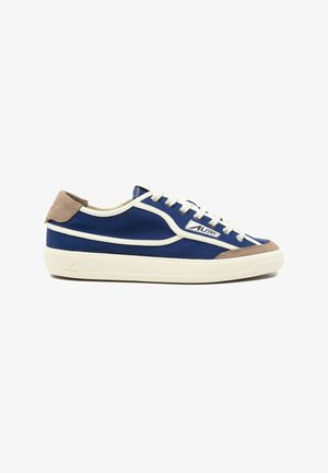 Zapatilla baja de lona azul con ribete blanco, detalles en ante beige en talón y puntera, cordones blancos y suela de goma blanca.