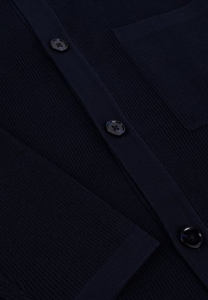 Donkerblauwe cardigan met geribbelde textuur, voorzien van zwarte knopen, een borstzak en een klassieke knoopsluiting.