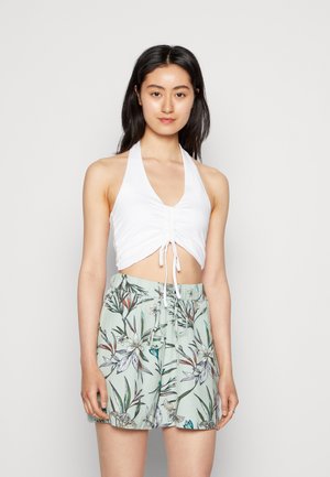 Top cropped branco com alças, apresentando detalhe franzido na parte frontal, combinado com calções verde claros com um padrão floral em tons de verde e azul.