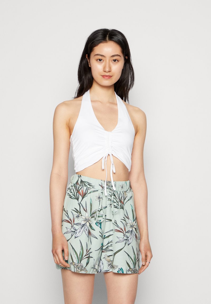 Top cropped branco com alças, apresentando detalhe franzido na parte frontal, combinado com calções verde claros com um padrão floral em tons de verde e azul.