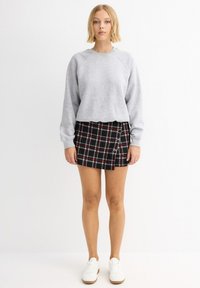 Sudadera gris con mangas raglán, combinada con una mini falda a cuadros negra y roja que presenta detalles circulares plateados y una abertura lateral.