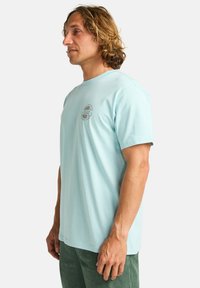 T-shirt di cotone azzurro chiaro con maniche corte e scollo rotondo, caratterizzato da un logo circolare nella zona sinistra del petto.