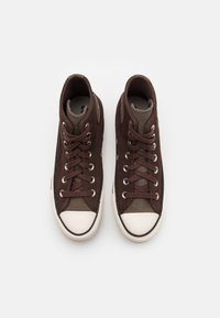 Braune High-Top-Sneaker aus Wildleder mit einem kontrastierenden grauen Stoffbereich, weißer Gummikappe und braunen Schnürsenkeln durch silberne Ösen.