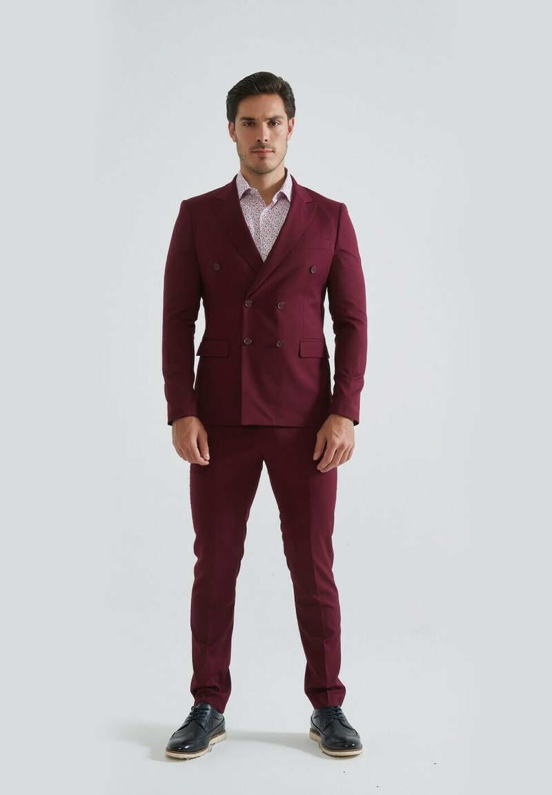 Costume bordeaux à double boutonnage avec un pantalon slim, associé à une chemise claire à motifs et des chaussures noires. Tissu lisse, design taillé.