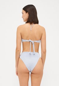 Világoskék bikini szett, amely nyakba akasztós dizájnnal és megkötős hátkiképzéssel rendelkezik. Magas derekú alsó rész, sima textúrával és minimális részletezéssel.