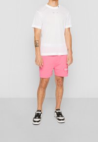 Bílý síťovaný tričko s krátkým rukávem, na kterém je barevný text. V páru s růžovými šortkami, které mají logo. Černobílé tenisky.