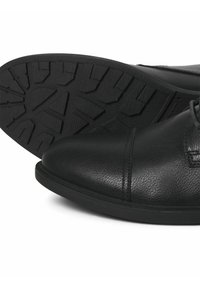 Zapatos de cuero negros con punta redonda y suela de goma texturizada. Presentan costuras visibles y un diseño de cordones.