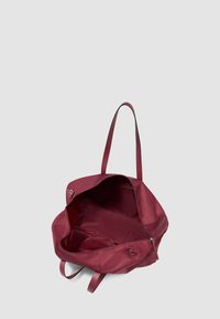 Bolso tote abierto de color burdeos oscuro con largas correas para el hombro y una cremallera, mostrado vacío sobre un fondo gris claro.