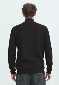 Maglione nero a costine con maniche lunghe e colletto alto, caratterizzato da un tessuto testurizzato e una silhouette aderente, vista dal retro.