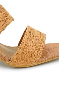 Tanan geweven sandalen met twee brede banden met bloemmotieven, een platte zool en een textuur voetbed voor comfort.