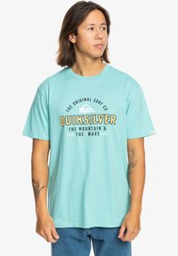 Turquoise cotton t-shirt featuring a central graphic in black and yellow text. Short sleeves and a rounded neckline. Casual fit.