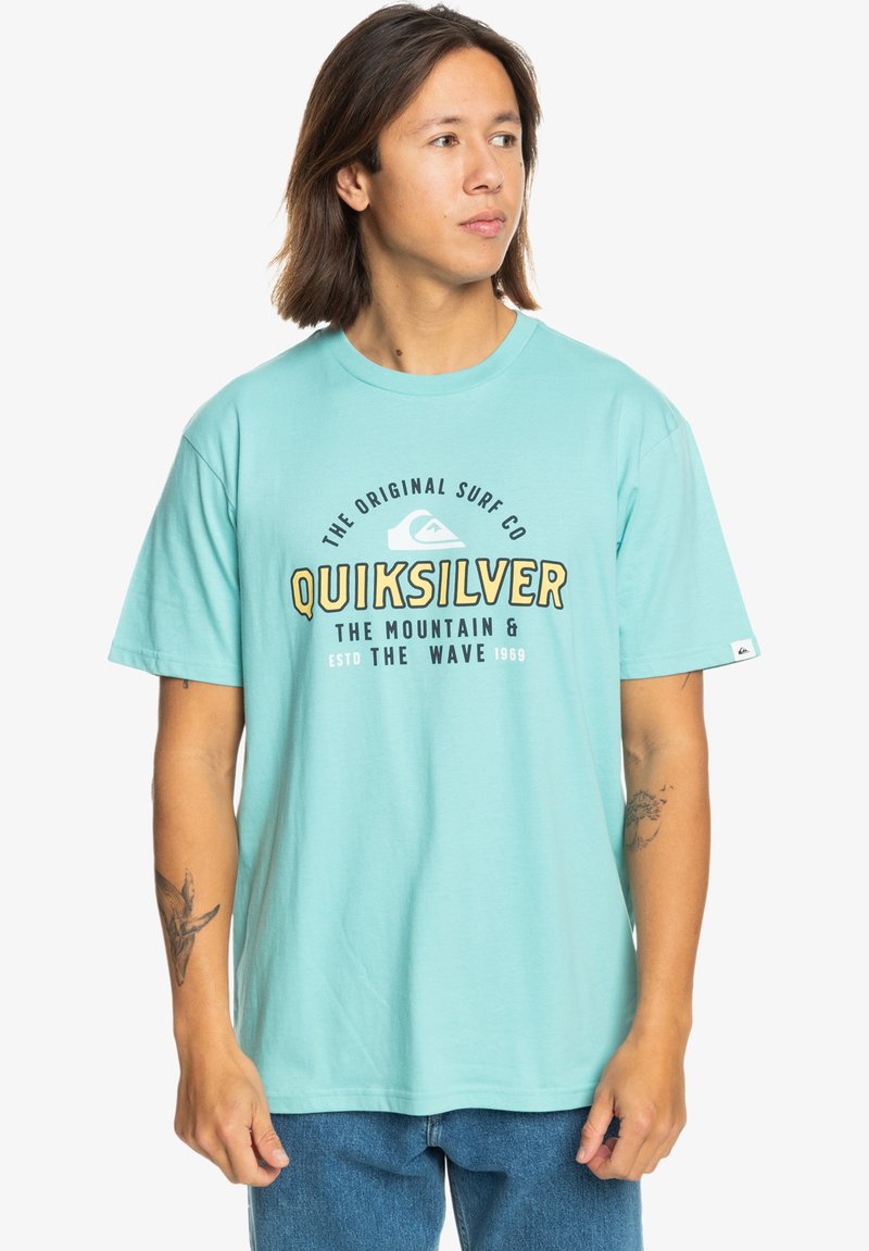 Turquoise cotton t-shirt featuring a central graphic in black and yellow text. Short sleeves and a rounded neckline. Casual fit.