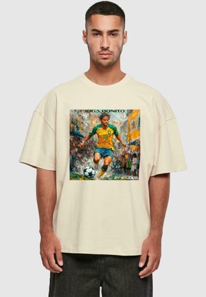 Beige oversized t-shirt featuring a colorful graphic of a soccer player in a yellow and green uniform, with the text "JOGA BONITO" above.