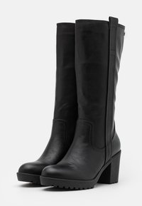 Bottines noires montantes en cuir lisse, avec un talon bloc haut et effilé et une semelle en caoutchouc texturé. Présente des coutures latérales et une languette.