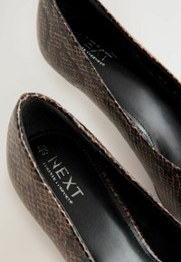 Braune Stiefeletten aus Kunstleder mit Schlangenoptik, abgerundeter Vorderkappe und glattem schwarzen Innenfutter; mit dem Markennamen "NEXT" in der Nähe der Ferse.