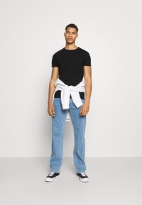 Svart kortermet t-skjorte, lyseblå rette jeans, hvit hettegenser knyttet i livet, svarte joggesko med hvite såler.