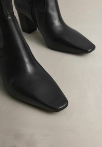 Zwarte leren enkelboots met spitse neuzen en een blokhak. Glad textuur met een strak ontwerp. Ritsluiting aan de zijkant.