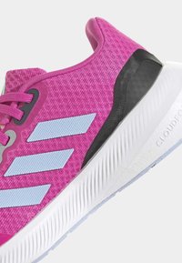 Scarpa sportiva rosa con tomaia in rete testurizzata, caratterizzata da tre strisce azzurro chiaro, contrafforte nero e suola bianca con design rigato.