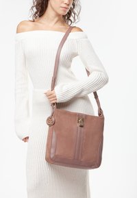 Bruine suède handtas met een glanzende roze lederen schouderband en gouden accenten. Voorzien van een verticale streepdessin en een ronde hangeraccent.